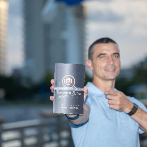 Jimmy Ricard holding a copy of Relearn2Live toward the camera on a boardwalk