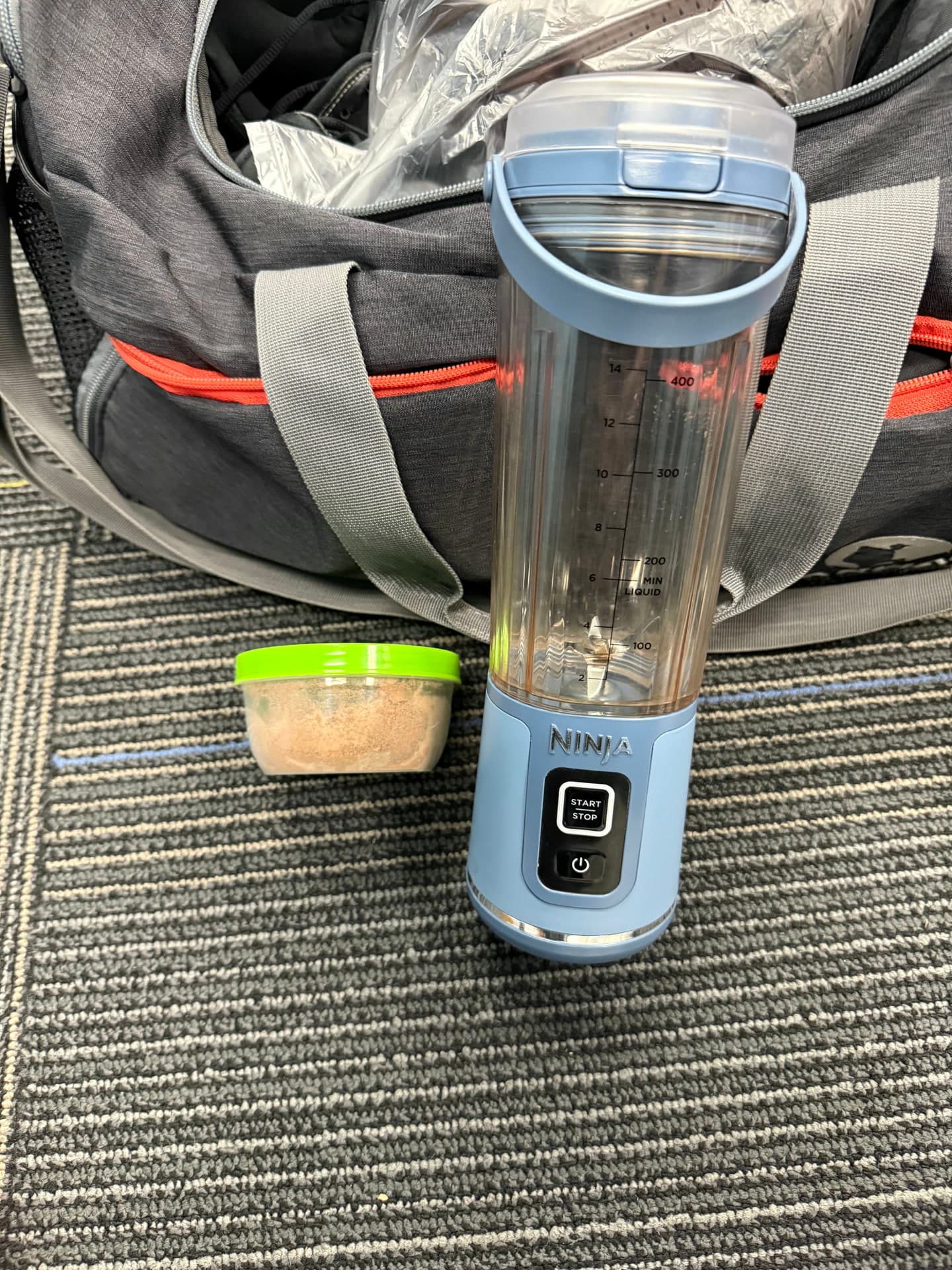 My blue portable blender and green-lidded portion cup beside my gym bag